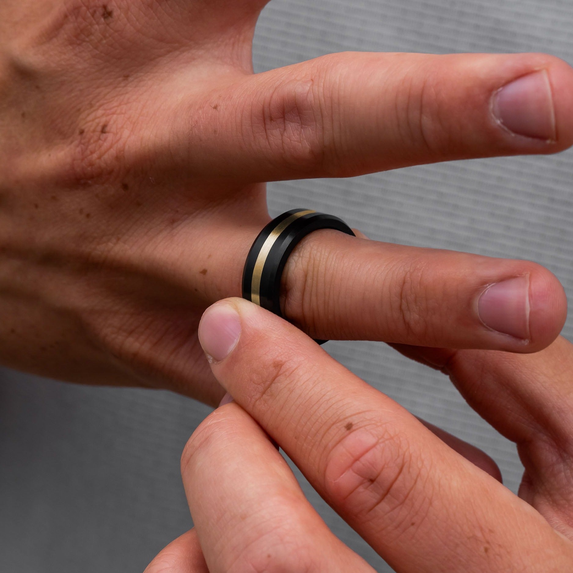 Lifestyle shot #1 of men's hands wearing our Elysium ARES Men's Black Diamond & 14k Yellow Gold Inlay | ElysiumBlack.com | Men’s 14k Yellow Gold Inlay Wedding Rings