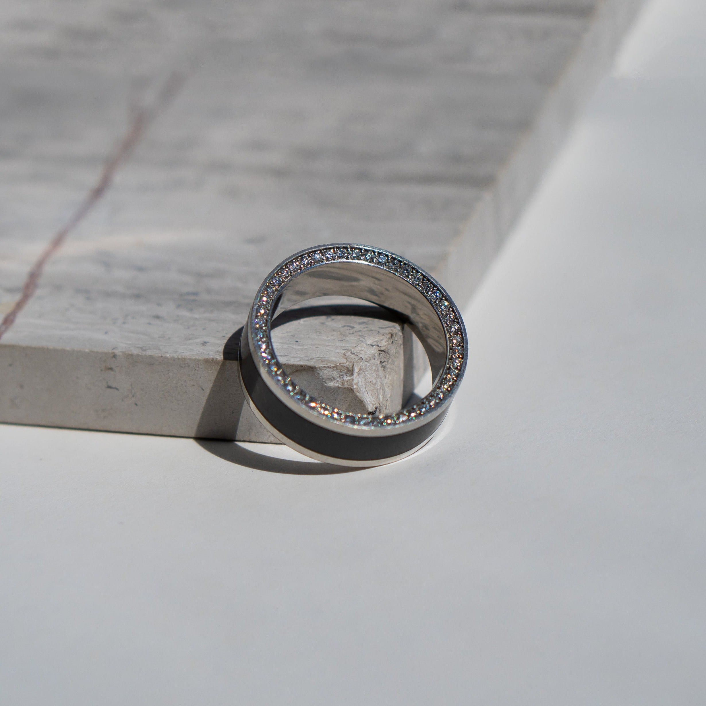 Ring shot #1 of our Elysium Zeus solid black diamond inlay ring with white diamond insets on a marble surface | Men’s Black Diamond Platinum Rings