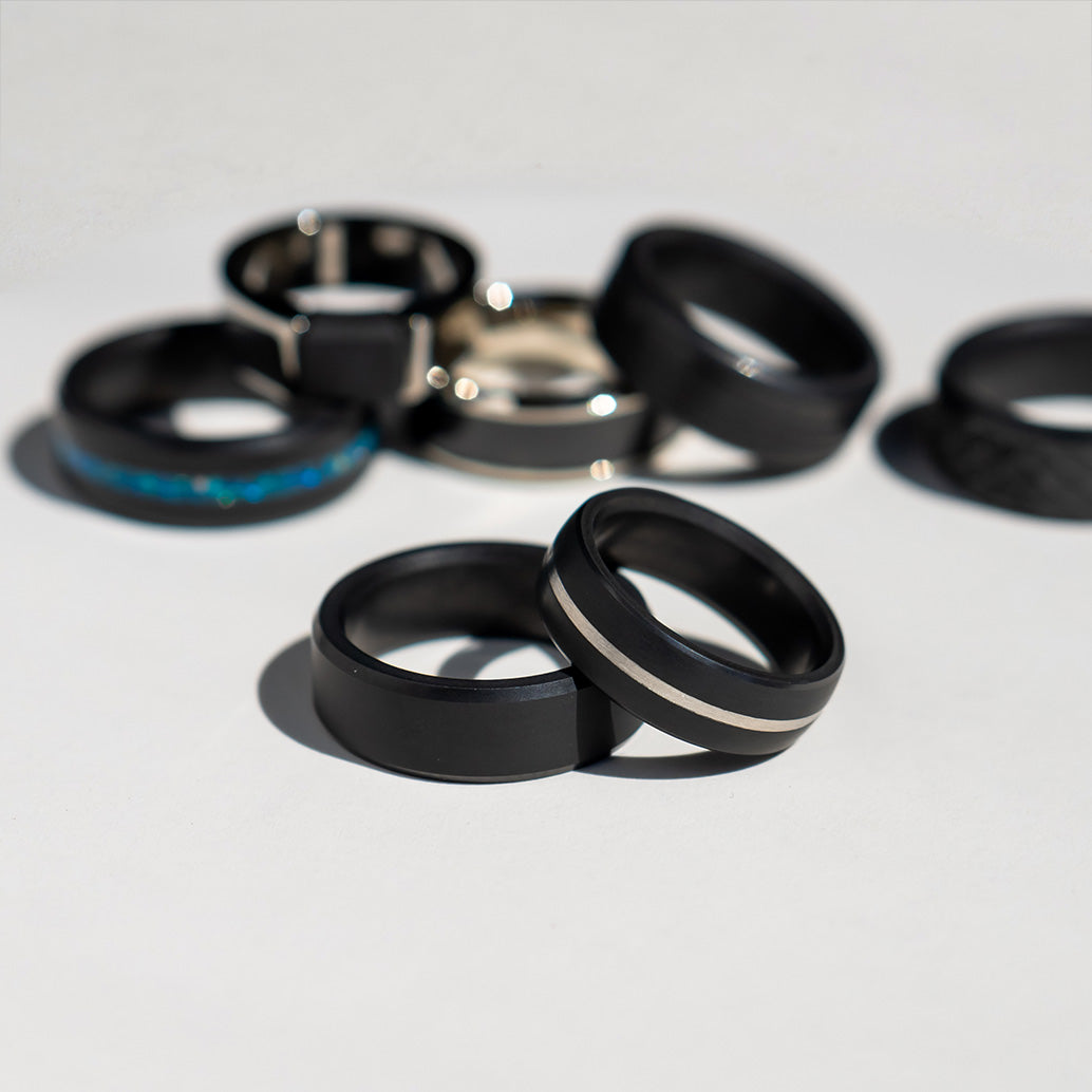 Display of Seven Different Black Diamond Wedding Bands with Yellow Gold, White Gold, & Blue Inlays | Men's Rings | 8mm Elysium Black Diamond Rings | Collections