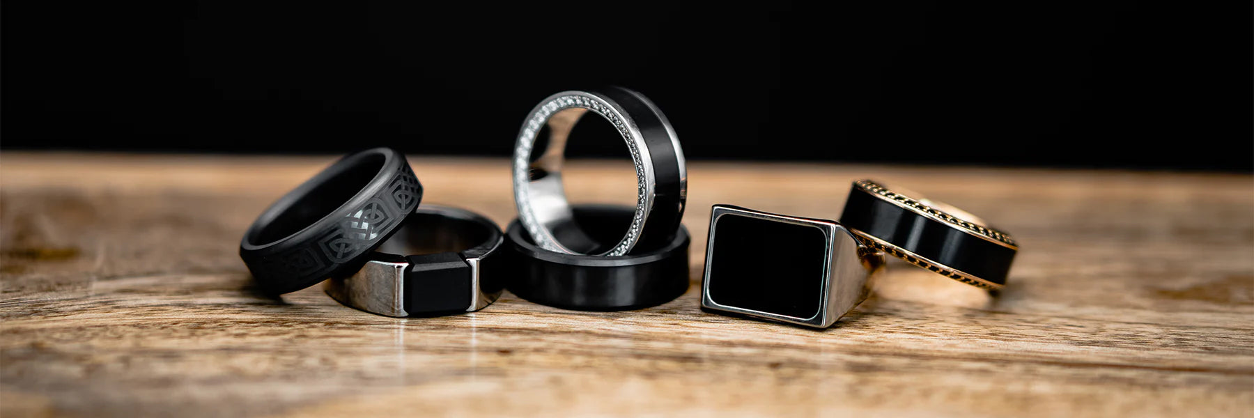 Six Different Black Diamond Rings on Wood Surface | Display of Black Diamond Wedding Rings with Yellow Gold, Silver, & White Gold | All Elysium Black Diamond Rings | Collections