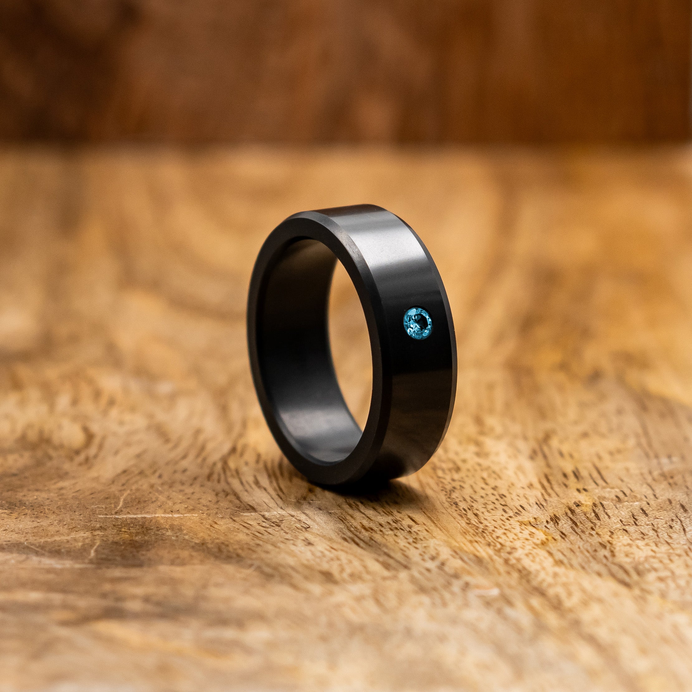 Ring shot #1 of our Elysium ARES Men's Black Diamond & Blue Diamond Inset resting on a wood surface | ElysiumBlack.com | Men’s Blue Diamond Wedding Rings