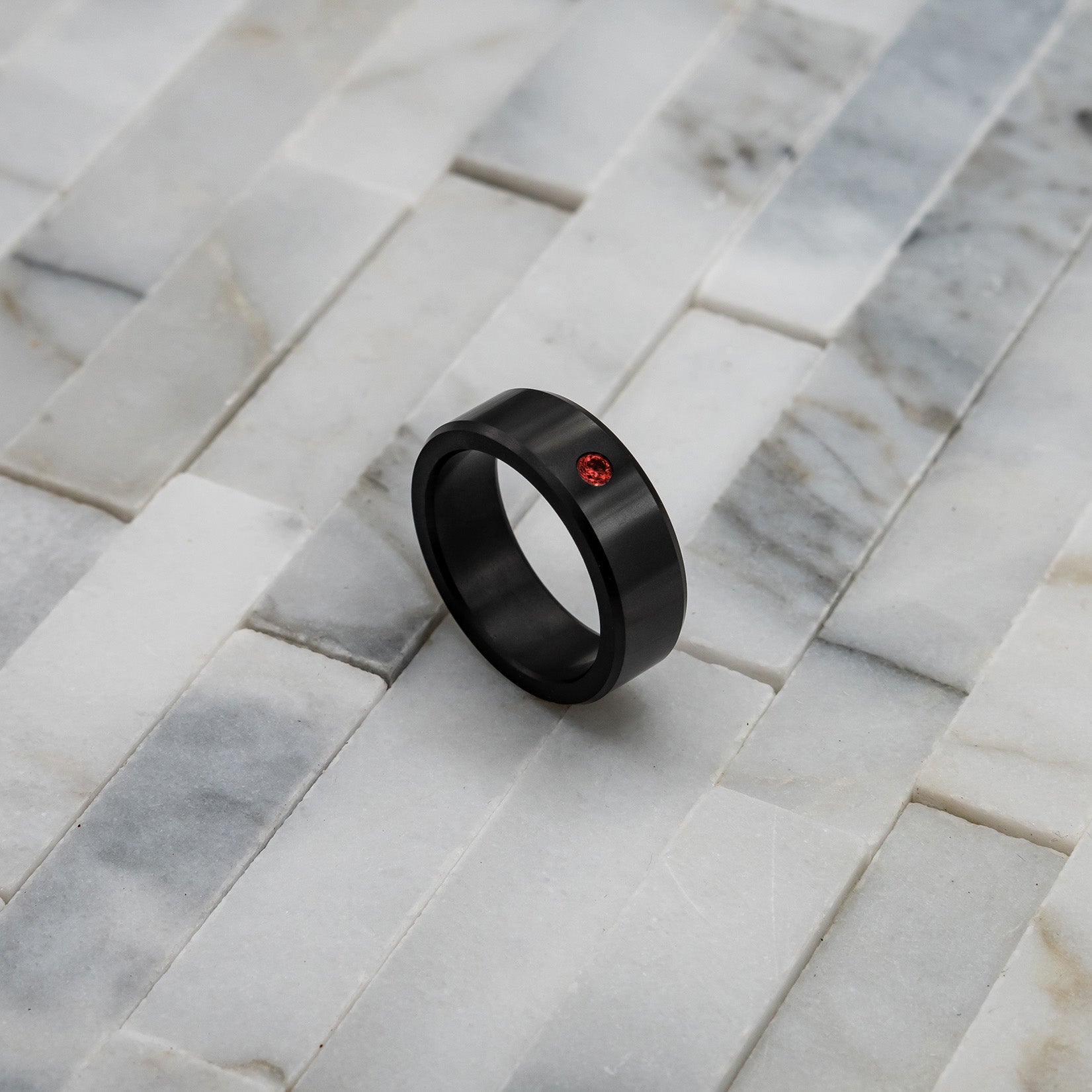 Ring shot #1 of our Elysium ARES Men's Black Diamond & Red Diamond Inset resting on a marble surface | ElysiumBlack.com | Men’s Red Diamond Wedding Rings